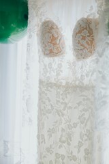 White bridal dress near the window with green balloons on the wall