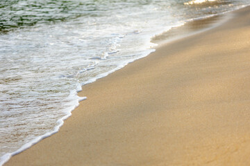 Selective focus of sand beach with sea wave, White bubbles on shoreline while sea wave approaching, Sand texture with free copy space, Beautiful nature pattern background.