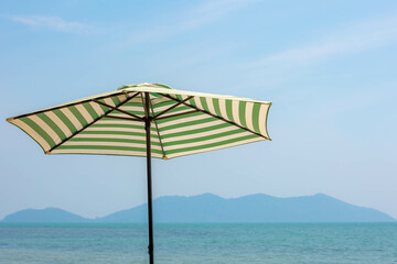Sun protection from concept, Classic vintage pool umbrella under blue clear sky in summer, Fabric umbrella pole on the seaside with blurred Islands as background, Relaxation and rest under shade.