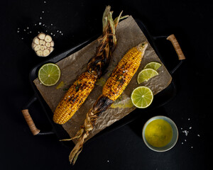 Grilled sweet corn cobs with garlic butter and lime on a dark gray stone background. Mexican street...