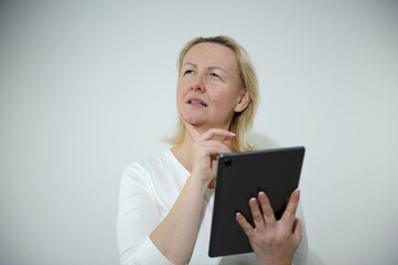 adult woman with tablet in hands thoughtfully supports chin with finger looks up to order