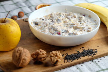 Homemade granola with yogurt for breakfast in a white bowl. Fresh banana, apple on wooden table. Health food concept.
