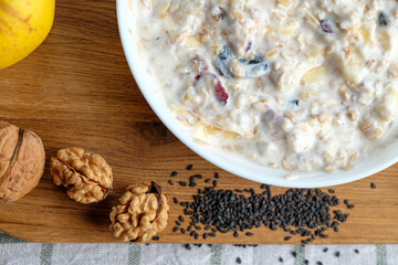 Homemade granola with yogurt for breakfast in a white bowl. Fresh banana, apple on wooden table. Health food concept.
