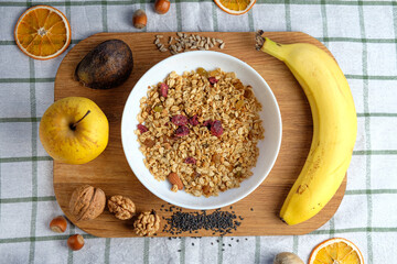 Granola with cranberries and almonds in a white bowl . Fresh banana and apple, walnut, seeds  on wooden table.   Health food concept. Breakfast food background
