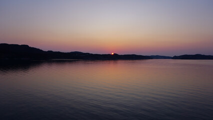 Colorful sunset over a lake, bits of land and mountains in the background