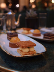 Close up of traditional French millefeuille stuffed with vanilla cream on table with other dessert and pot in background. It is a dessert made of puff pastry layered with pastry cream