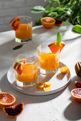 Glasses of freshly squeezed juice with leaves and fruits on table on bright background. Grapefruits, oranges, bloody oranges, kumquats and ice cubes.