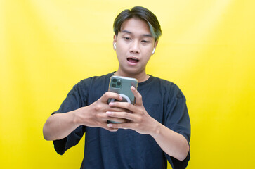 An enthusiastic Asian man with peek-a-boo hair is using airpods while dancing joyfully, checking his phone, and listening to music.