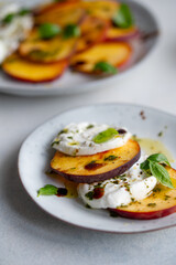 Italian Caprese salad with peaches, buratta cheese, herbs and balsamico creme. Fresh gourmet salad on a plate on white stone background