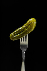 Pickled cucumber on a fork on a black background