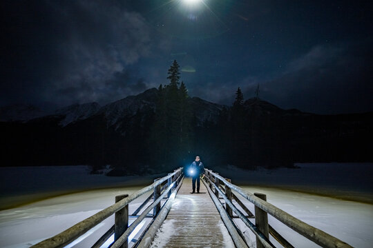 man with flash light at night on wooden bridge of pyramid lake in jasper national park
