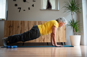 Active senior man in bright yellow shirt exercising at home making a plank position