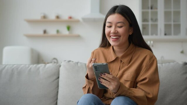 Asian woman winner holding smartphone get free prize winning online in app. Excited korean chinese girl businesswoman using phone celebrate lottery money win mobile victory yes gesture success at home