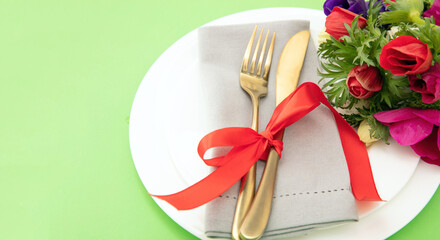 Spring table setting, Wild flowers decoration, napkin and cutlery on plates, pastel green background,