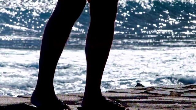 Legs of a man wearing flip-flops at the sea side, big waves in background in a blue sea