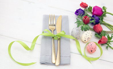 Easter table setting, Spring flowers and eggs decoration, napkin and golden cutlery on white wood