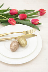 Easter table setting, Red tulips and eggs, golden cutlery on plates, white background