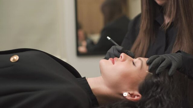 A woman master makes permanent eyebrow makeup to a young beautiful girl in a beauty salon.Microblading, eyebrow tattoo in a beauty salon.