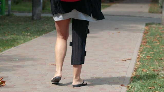 Disabled woman with with orthosis knee brace on leg walking outdoors. Rehabilitation, knee injury, meniscus injury, tendon rupture, exoskeleton concept