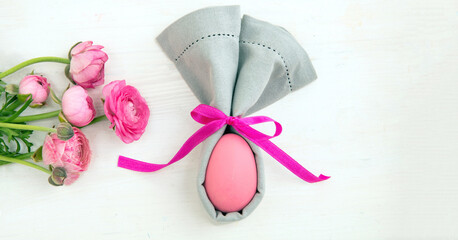 Easter table setting, Pink Easter egg in a gray napkin, rabbit ears shape on white wood