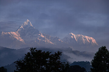 View of Machapuchare (Fish-Tial) mountain at foggy sunrise, situated in the Annapurna mountain massif, North of Pokhare, as seen from Pokhara, Nepal Himalayas, Nepal