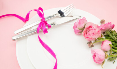 Spring Holiday table setting, Pink buttercup flowers and cutlery on white plates, closeup