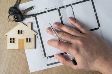 Architect, interior designer or real estate agent hand holding pen. Showing home floor plans. Working on flat or apartment building blueprints project. Design concept with wooden model house and keys.