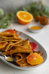 Fototapeta na wymiar Traditional French Crêpes suzette pancakes with orange sauce on a serving dish on a light grey tale background decorated with citruses and bloody oranges. 