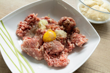 Minced meat, egg, onion and spices in a bowl. Preparing minced cutlets in Poland, traditional Polish kotlety mielone. Roll dipped in milk in background.