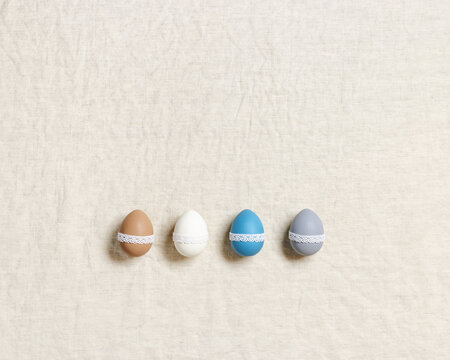 Decorated Easter eggs, various pastel colors and white tape lace, traditional holiday food on linen table, rustic background. Set colorful chicken egg for Happy Easter. Minimal Flat lay