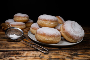 Pączki deep-fried Polish doughnuts and mini strainer with powdered sugar. Celebrating Fat Thursday, Tłusty czwartek feast, traditional day in Poland. Pączek food, filled with rose hip jam.