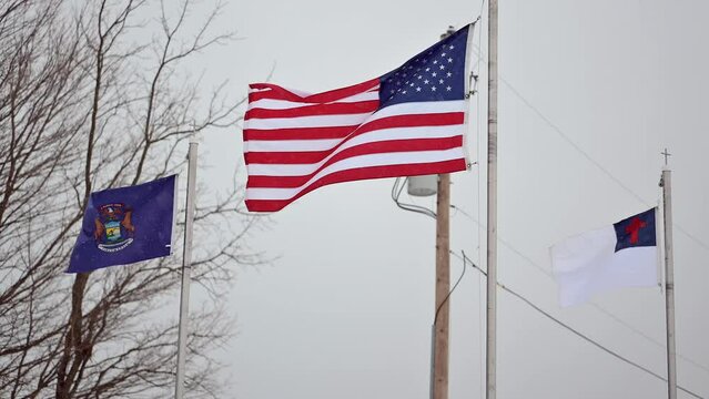 American flag, Christian flag, and Michigan flag waving in the wind in winter