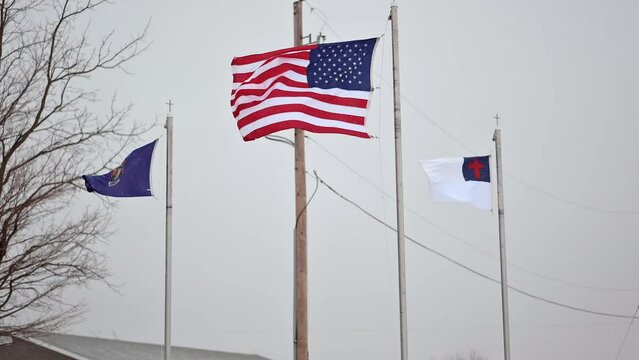 American flag, Christian flag, and Michigan flag waving in the wind in winter