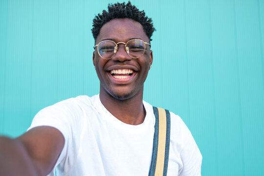 Selfie of cheerful handsome man in the street. Portarit of happy young man doing a selfie photo on the camera on a turquoise background wall.