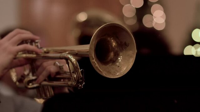 Musician playing golden trumpet with the orchestra against a blurred background with bokeh lights