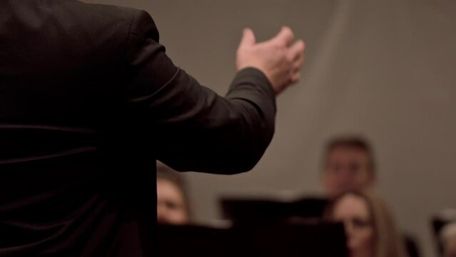 Selective focus of the choir director in a black suit leading the choir by moving his hands