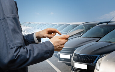 Hands with digital tablet on a background of rows of cars. Car sales.