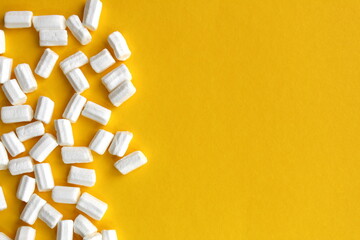 Background of white small marshmallows scattered on a yellow background.