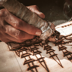 An artist using a pyrography tool to create a pyrogravure. Wood burning with pyrography pen. 