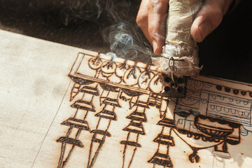 An artist using a pyrography tool to create a pyrogravure. Wood burning with pyrography pen. 