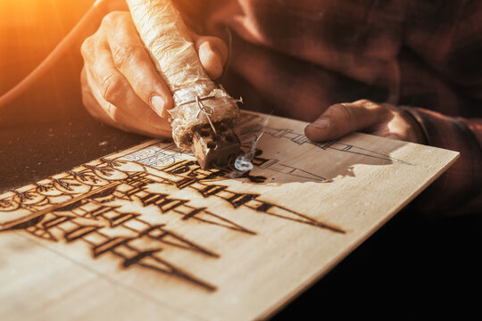 An artist using a pyrography tool to create a pyrogravure. Wood burning with pyrography pen. 