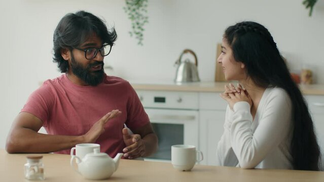Indian couple talking sitting at dining table communicate indoors muslim arabian man tell story speaking to woman diverse boyfriend and girlfriend discussing future plans girl and guy talk in kitchen
