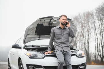 Sad driver calling car service, opening hood, having engine problem standing near broken car on the...