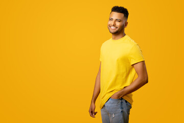 Handsome smiling Indian young man in yellow casual t-shirt posing on yellow background, charismatic...