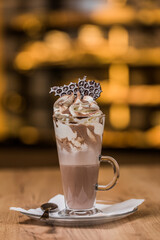 a glass of hot chocolate topped with whipped cream and cocoa powder and piece of bubble choclate