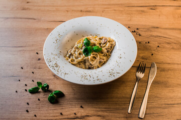 spaghetti carbonara on a white plate with basil leaves and peppercorns and silver cutlery on a side