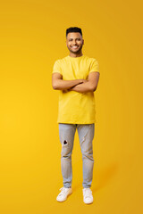 Fototapeta na wymiar Full size length portrait of confident happy young Indian man 20s in yellow t-shirt holding hands crossed isolated on plain yellow background, foreign male student