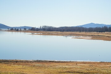 Scenic shot of the coast of a lake surrounded by hills under the blue sky