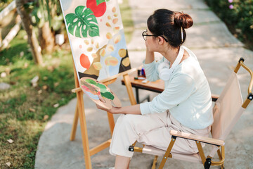 Young asian woman artist painting on canvas..Female artist drawing with inspiration in garden.