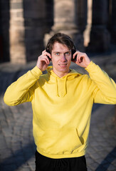 Smiling man in yellow sweatshirt with a headphones listening music outdoors